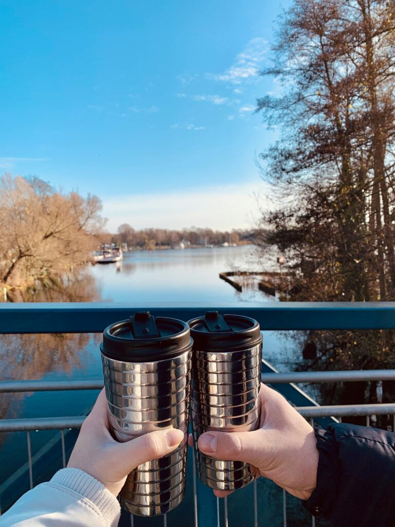pexels-photo-14011461-14011461 Two people holding reusable mugs by a serene lake on a sunny day.
