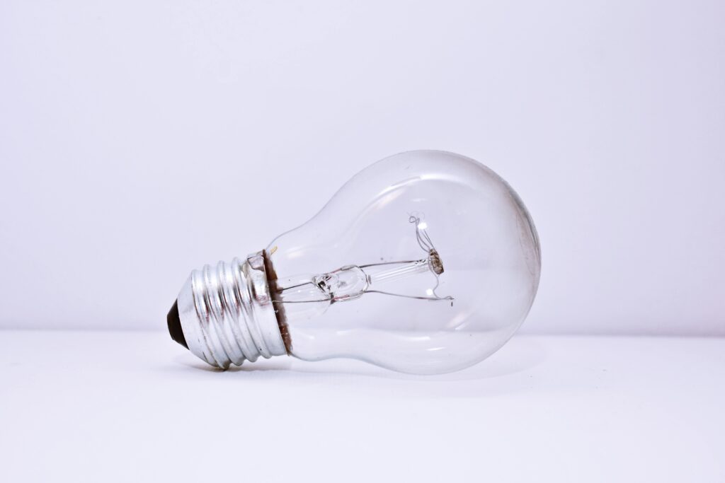 A clear incandescent light bulb lying on a simple white background, showcasing minimalism.