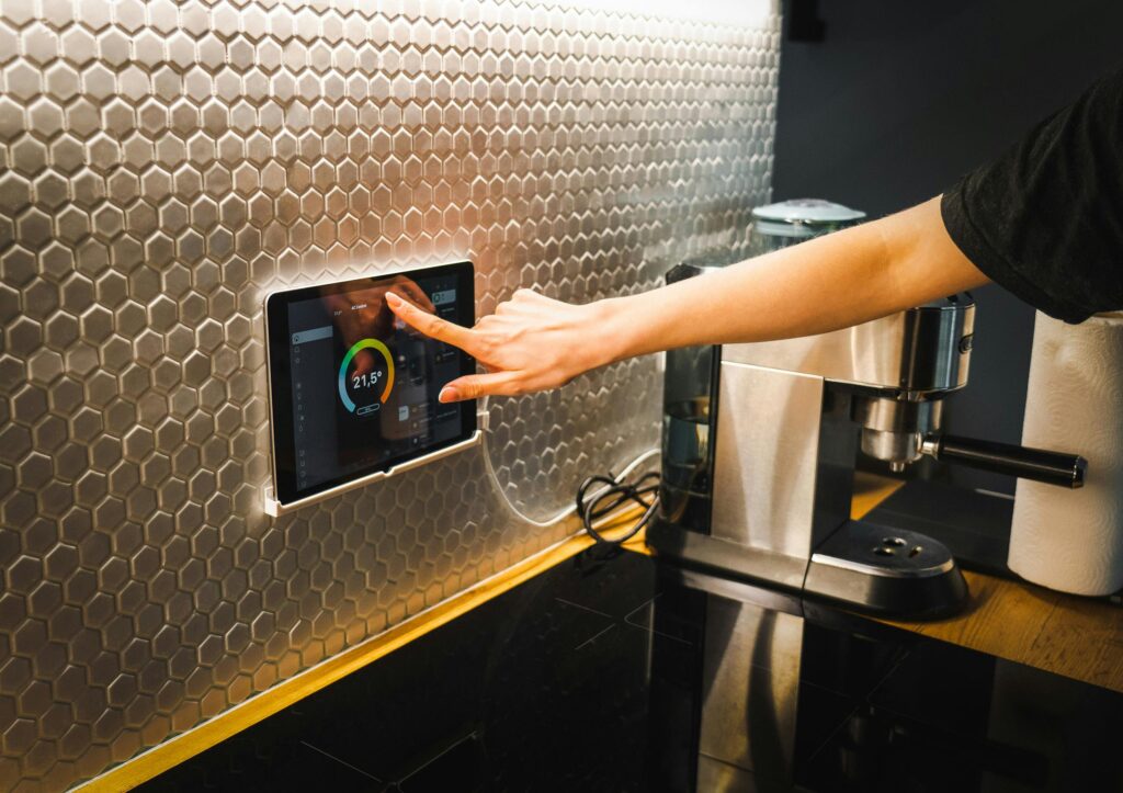 Modern kitchen scene featuring a hand using a tablet to control a smart home system.