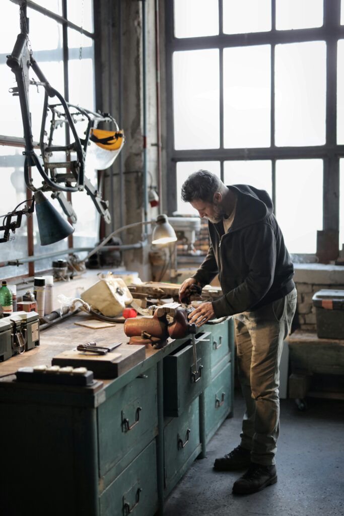 pexels-photo-3822900-3822900 Side view of bearded male master in casual clothes standing at workbench and fixing details with professional metal instrument