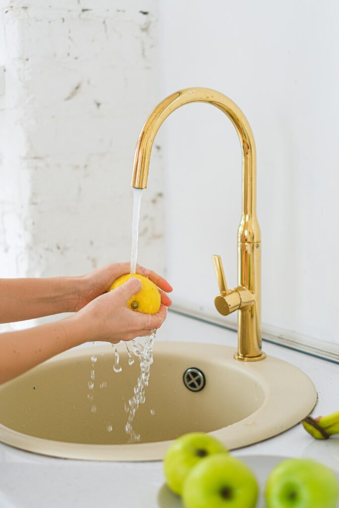 pexels-photo-6593605-6593605 Hands washing a lemon in a sink under running water with green apples nearby.