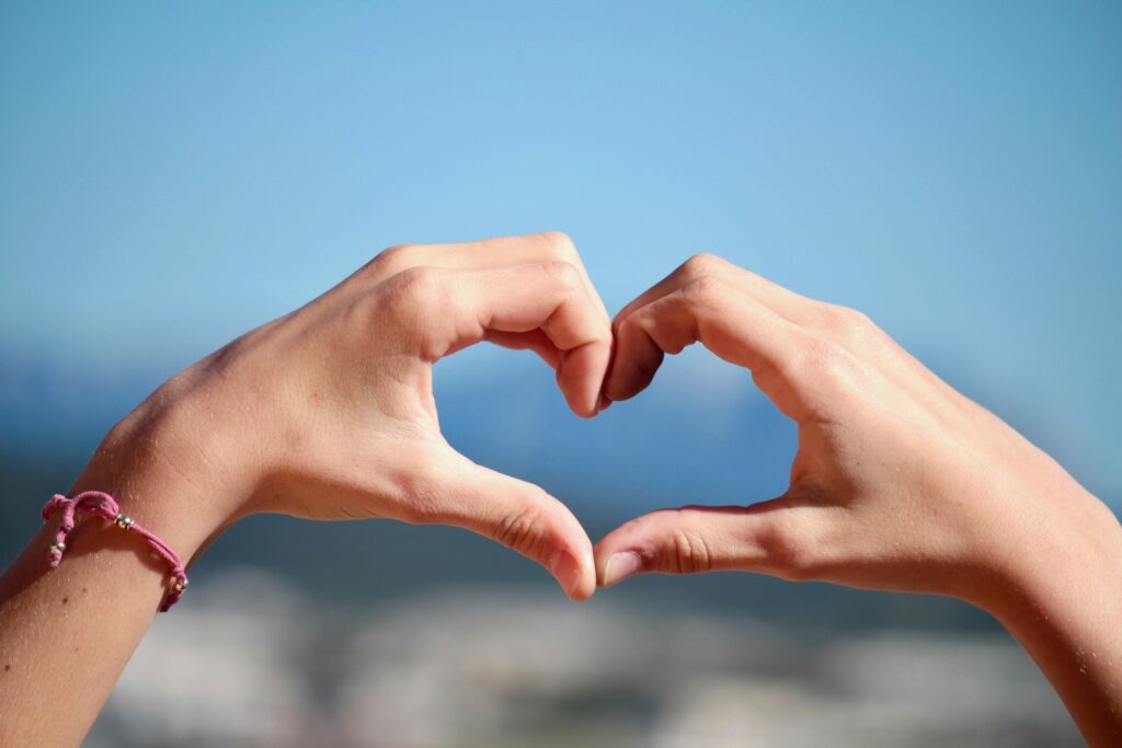 Close-up of hands forming a heart shape with clear blue sky background.