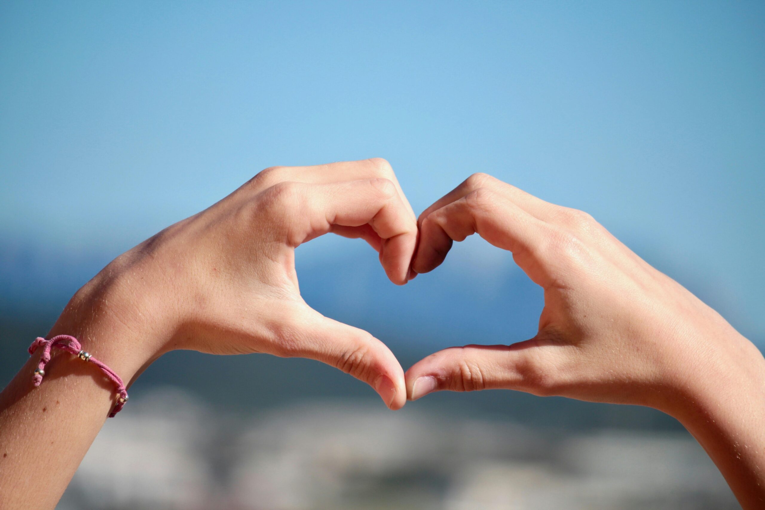 Close-up of hands forming a heart shape with clear blue sky background.